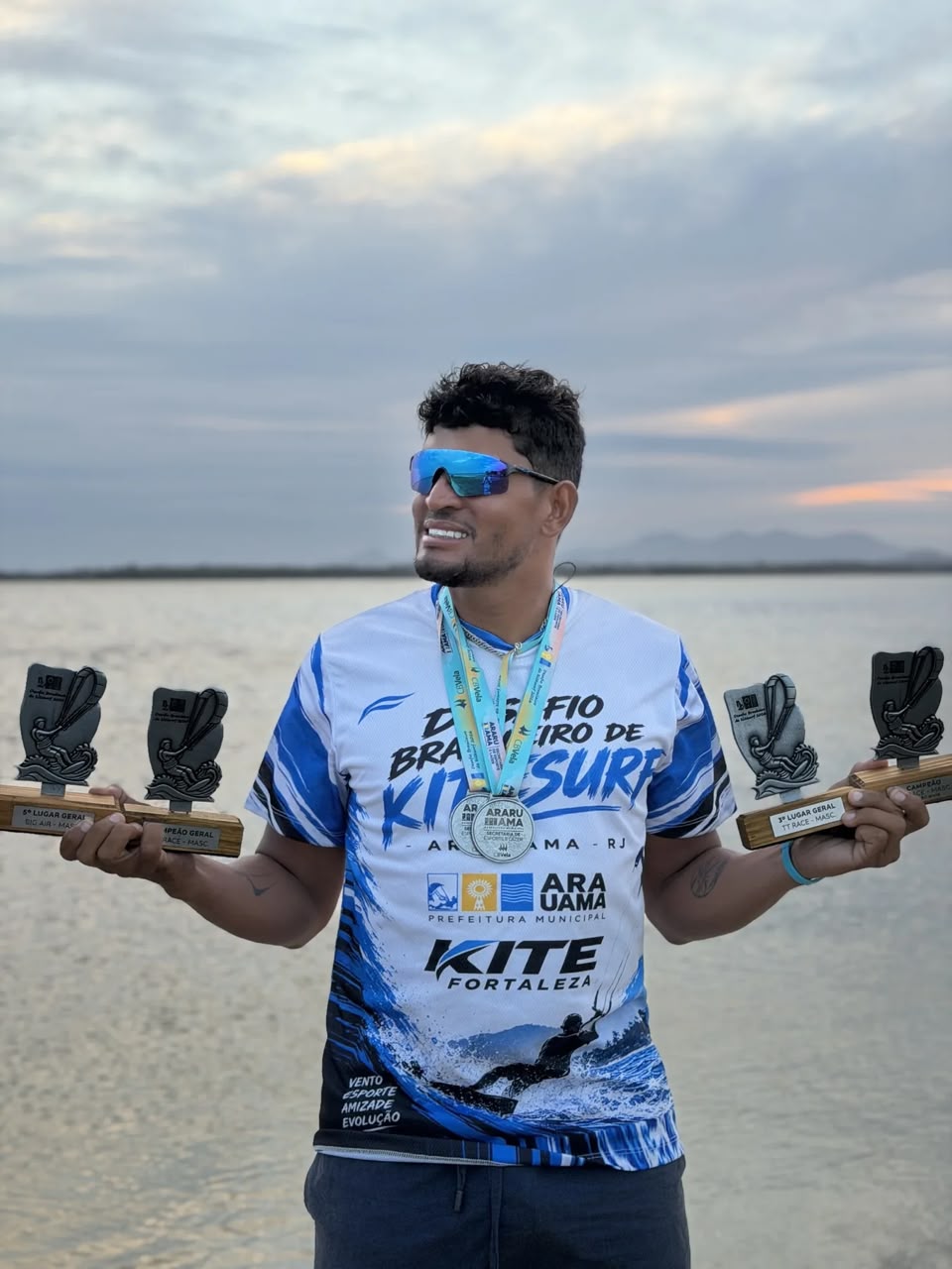 Raul segurando medalha e troféus de kitesurf na praia